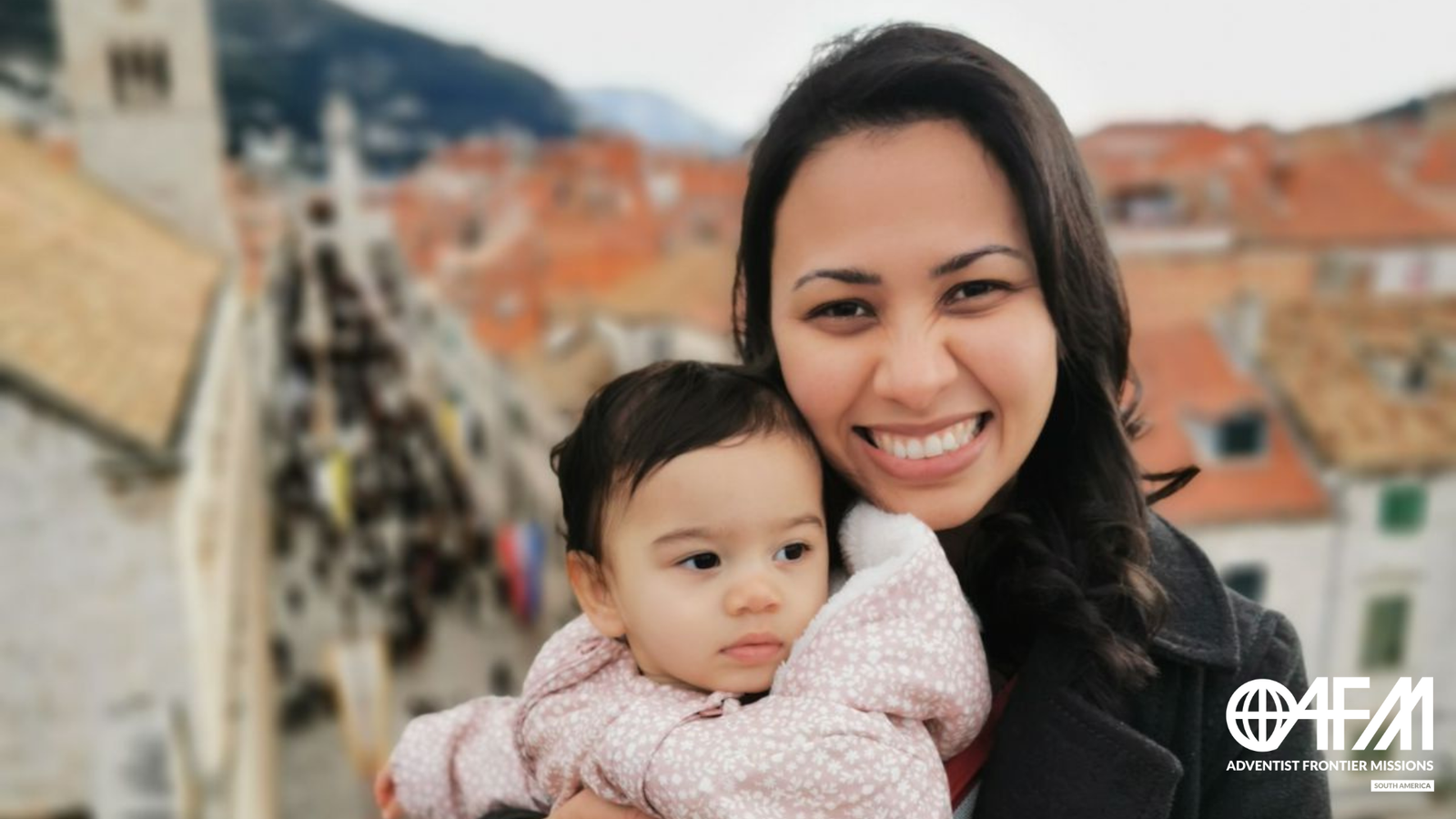 Missionária de carreira segurando sua filha nas muralhas de uma cidade medieval no Leste Europeu